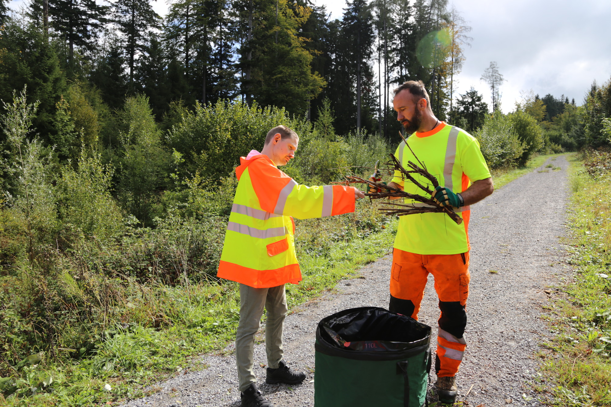 Christoph Otter und ein Klient sammeln entferntes Pflanzenmaterial an einem Waldweg