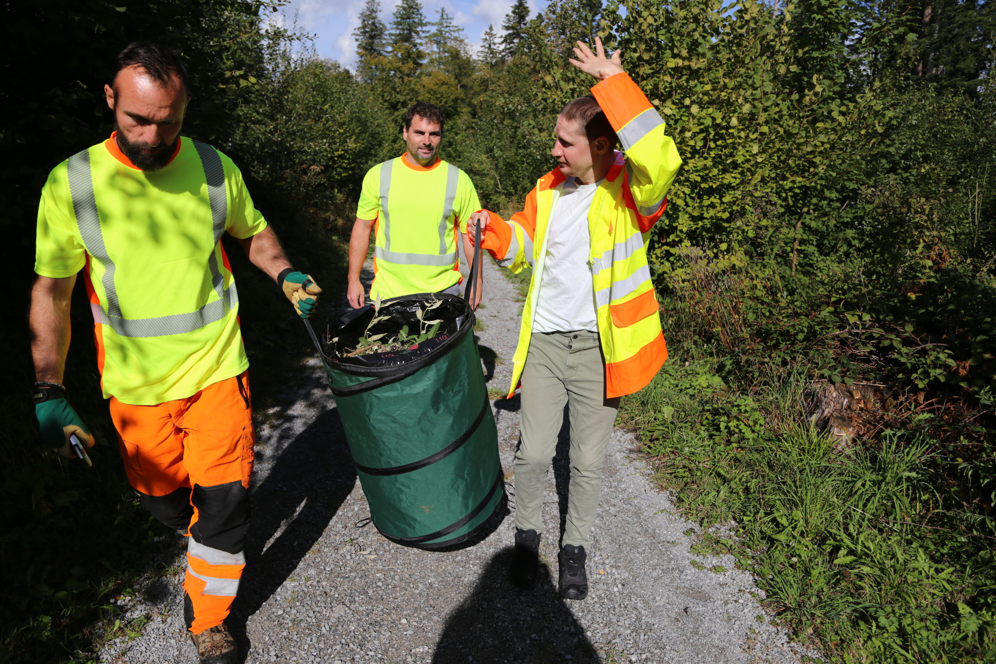 Drei Personen des EPI WaldWerks tragen gemeinsam einen mit Pflanzenmaterial gefüllten Behälter
